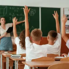 19 maja. Nauczycielka przy tablicy, uczniowie z podniesionymi rękami, gotowi do odpowiedzi.