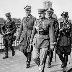 Marszałek Józef Piłsudski z braćmi w mundurach wojskowych idący w kolumnie.