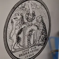 Herb z lwem i panterą, symbolizujący masonerię. Pod spodem napis "LOGE ZUM BEKRÄNZTEN CUBUS".