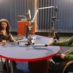 Kobieta i mężczyzna siedzą przy stole w studiu radiowym, gotowi do debaty.
