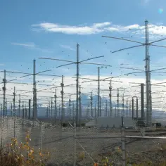 Ogromne pole anten HAARP pod błękitnym niebem, z górami w tle.