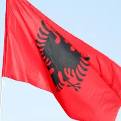 Czerwona flaga Albanii z czarnym dwugłowym orłem powiewa na tle błękitnego nieba.