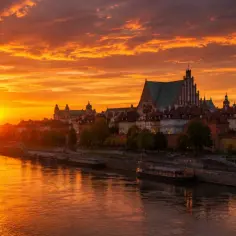 Zachód słońca nad Wisłą, kiedy jest najdłuższy dzień w roku. Złote niebo i odbijające się w wodzie światła tworzą magiczny widok Starego Miasta.