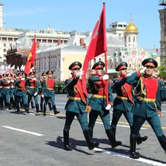 Uroczysta defilada wojskowa z okazji 9 maja. Żołnierze w historycznych mundurach maszerują z flagami na Placu Czerwonym.