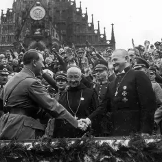 Hitler wita się z duchownym na tle tłumu i katedry w nazistowskich Niemczech.