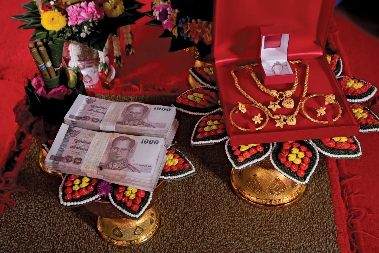 Złota biżuteria i stos banknotów 1000 bahtów na ozdobnych tacach. To symboliczny posag, często wręczany podczas ceremonii.