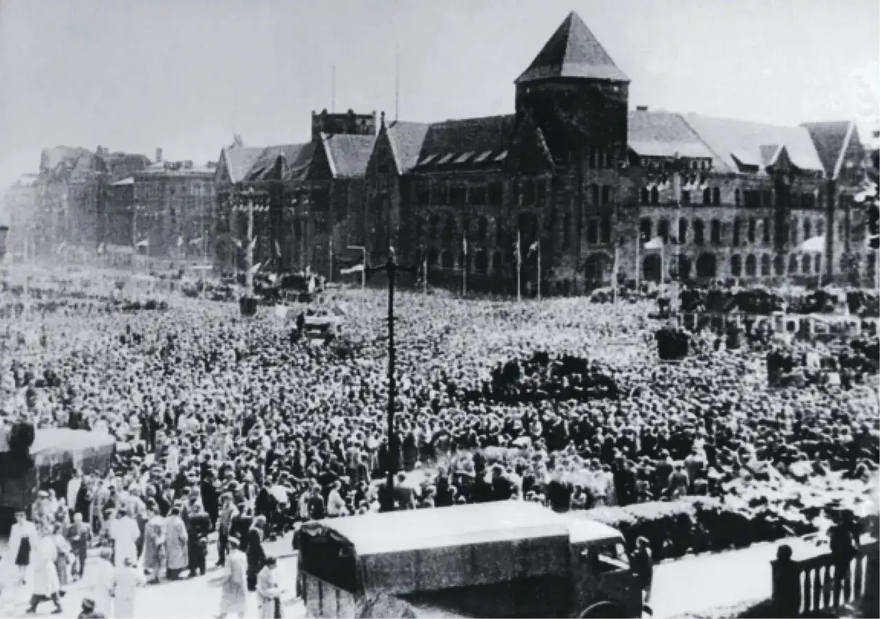 Tłum ludzi na placu przed budynkiem, prawdopodobnie wydarzenie z 1956 roku.