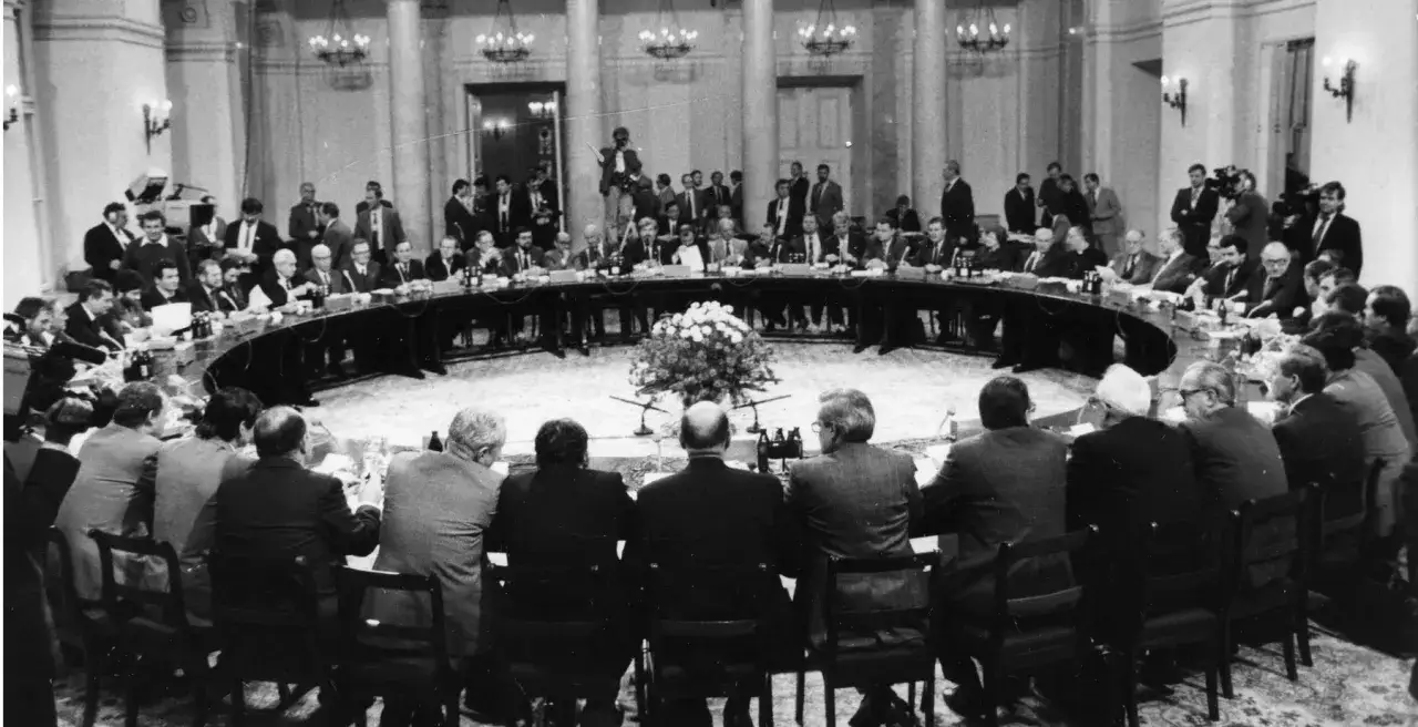 Okrągły stół, przy którym siedzą mężczyźni w garniturach. To historyczne spotkanie, które doprowadziło do powstania 3 Rzeczypospolitej.