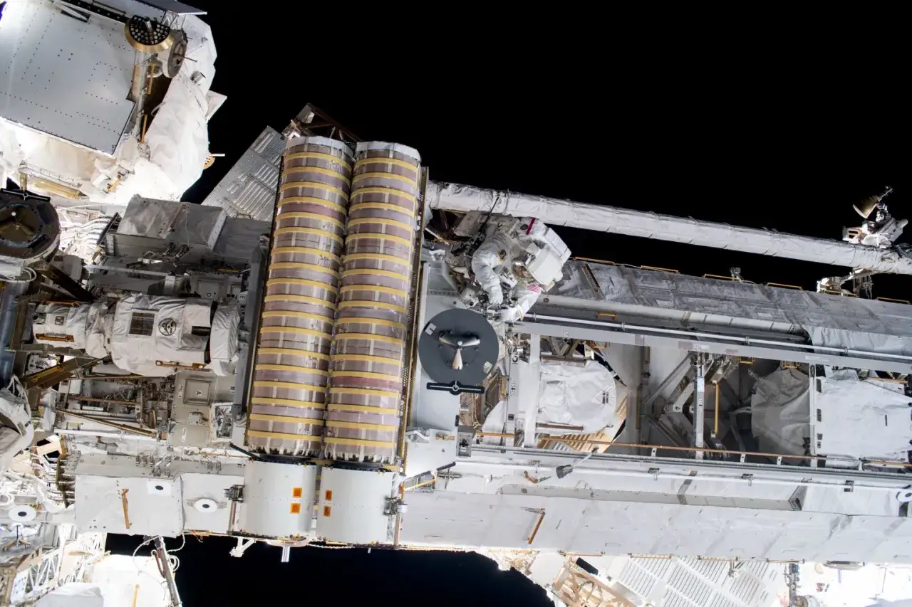 Astronaut pracuje przy Międzynarodowej Stacji Kosmicznej, która lśni w czerni kosmosu.