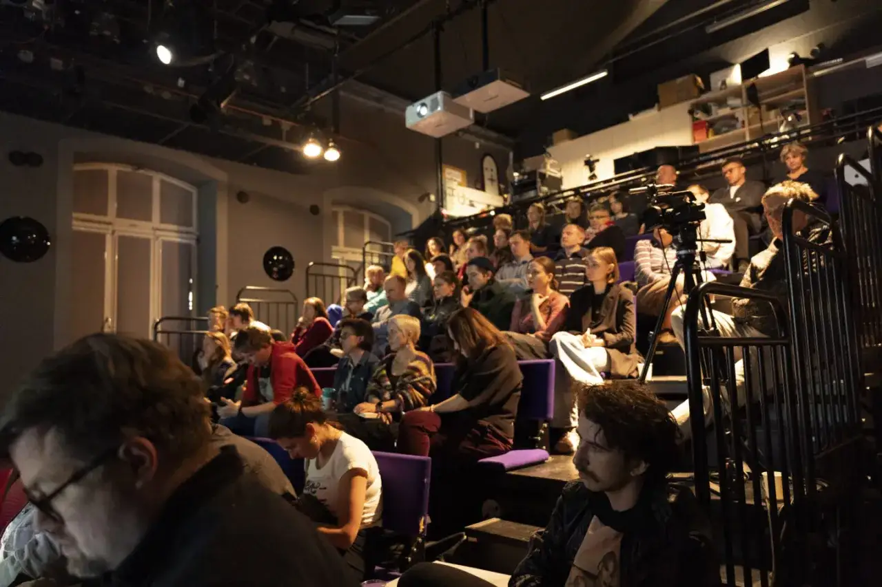 Widownia siedzi na widowni, gotowa na debatę. Kamera filmowa jest ustawiona, by uchwycić każdy moment.