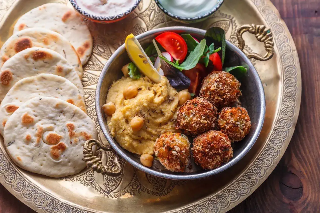 Pyszne, koszerne jedzenie: hummus, falafel, świeże warzywa i chlebki pita na ozdobnej tacy.