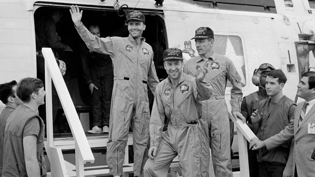 Astronauci misji Apollo 13 pozdrawiają. Widać ich w kombinezonach i czapkach z napisem 