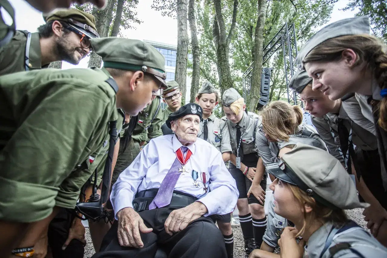 Szare szeregi harcerzy otaczają weterana z medalami.