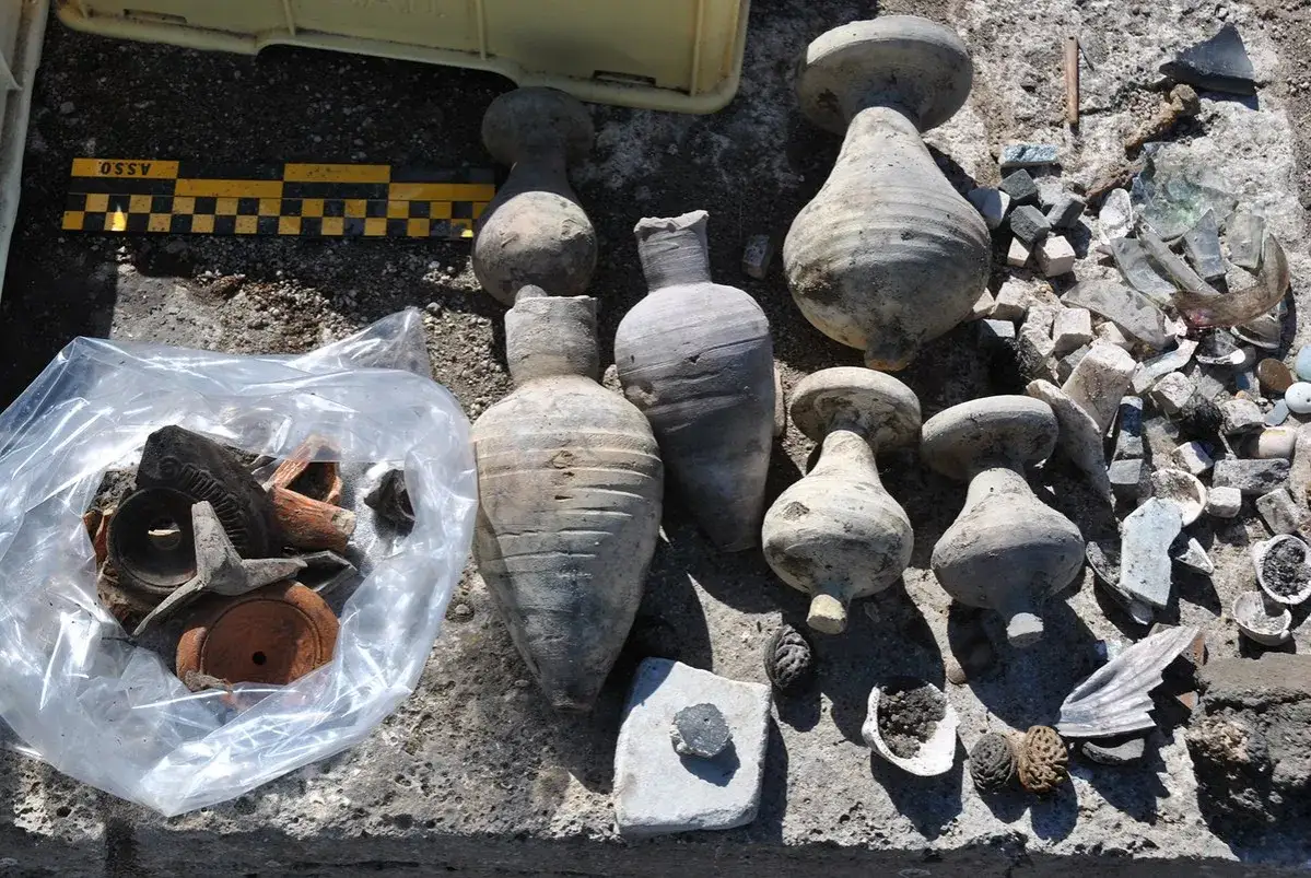 Archeolog odkrył starożytne naczynia i fragmenty ceramiki. Znaleziska leżą na ziemi obok plastikowej torby z innymi artefaktami.