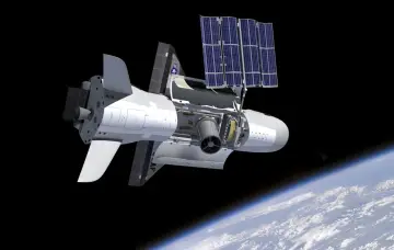 Bezkrytyczny X-37B w przestrzeni kosmicznej, z otwartym panelem odsłaniającym wnętrze i rozłożonymi panelami słonecznymi, nad Ziemią.